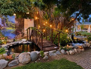 Un jardin agrémenté d’un pont en bois, d’un bassin et d’un éclairage décoratif.