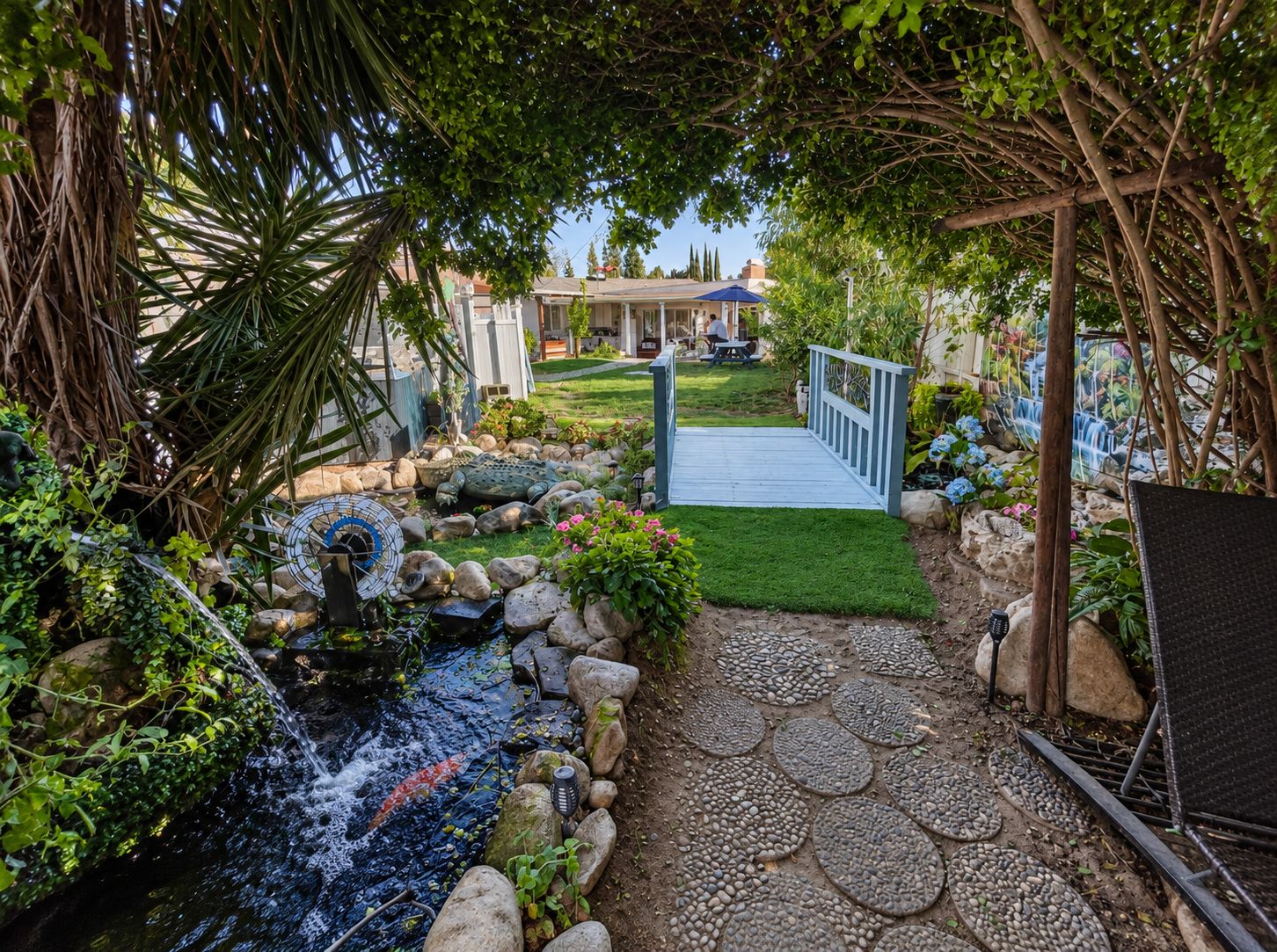 A garden with a water feature, a wooden bridge, and a patio area.