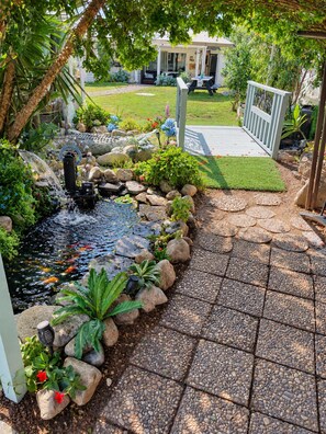 Un jardin agrémenté d’un élément aquatique, d’un chemin pavé et d’une maison en arrière-plan.
