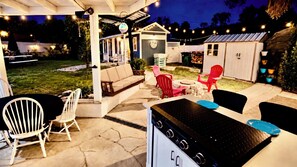 Une terrasse extérieure équipée d’une cuisinière à gaz, d’un espace salon et de guirlandes lumineuses.