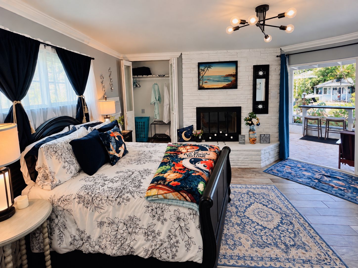 A bedroom with a bed, bedside table, lamp, and a view of the outdoors.
