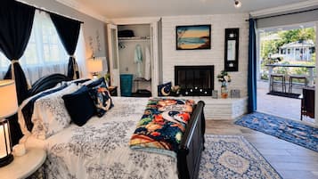 A bedroom with a bed, bedside table, lamp, and a view of the outdoors.