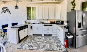A compact kitchen with white cabinets, a stainless steel refrigerator, a gas stove, and a patterned rug.