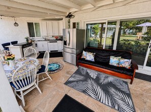 Un espacio habitable compacto con kitchenette, un comedor con mesa y sillas, un sofá con cojines y un ventanal corredero que da a un jardín.