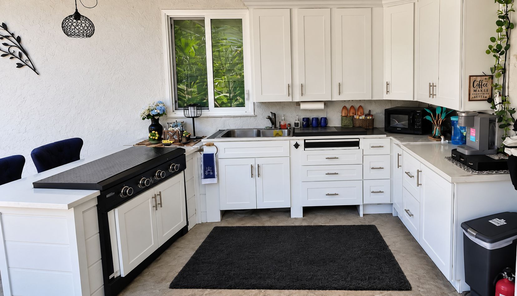 Een kleine keuken met witte kasten, een zwart aanrecht en een zwart vloerkleed.