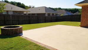 A backyard with a concrete patio, a brick fire pit, and a wooden fence.