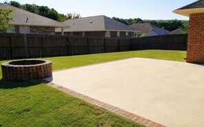 A backyard with a concrete patio, a brick fire pit, and a wooden fence.
