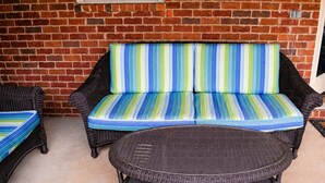 A wicker sofa with a striped cushion, a wicker table, and a brick wall in the background.