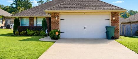 A residential house with a garage, a well-maintained lawn, and a trash bin.