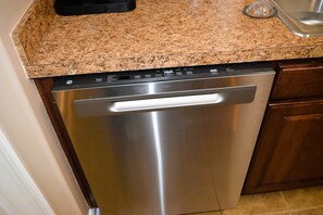 Un lavavajillas de acero inoxidable en una cocina con encimera de granito y armarios de madera.