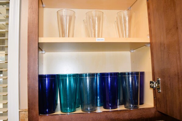 Un mueble de madera con dos estantes; el estante superior sostiene vasos de vidrio transparentes, y el estante inferior contiene vasos de vidrio azules.