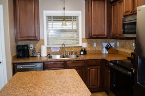 Una cocina con encimeras de granito, armarios de madera, horno empotrado y una ventana con persianas.