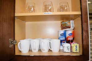 Un armario con copas de vino en el estante superior y tazas blancas en el inferior.