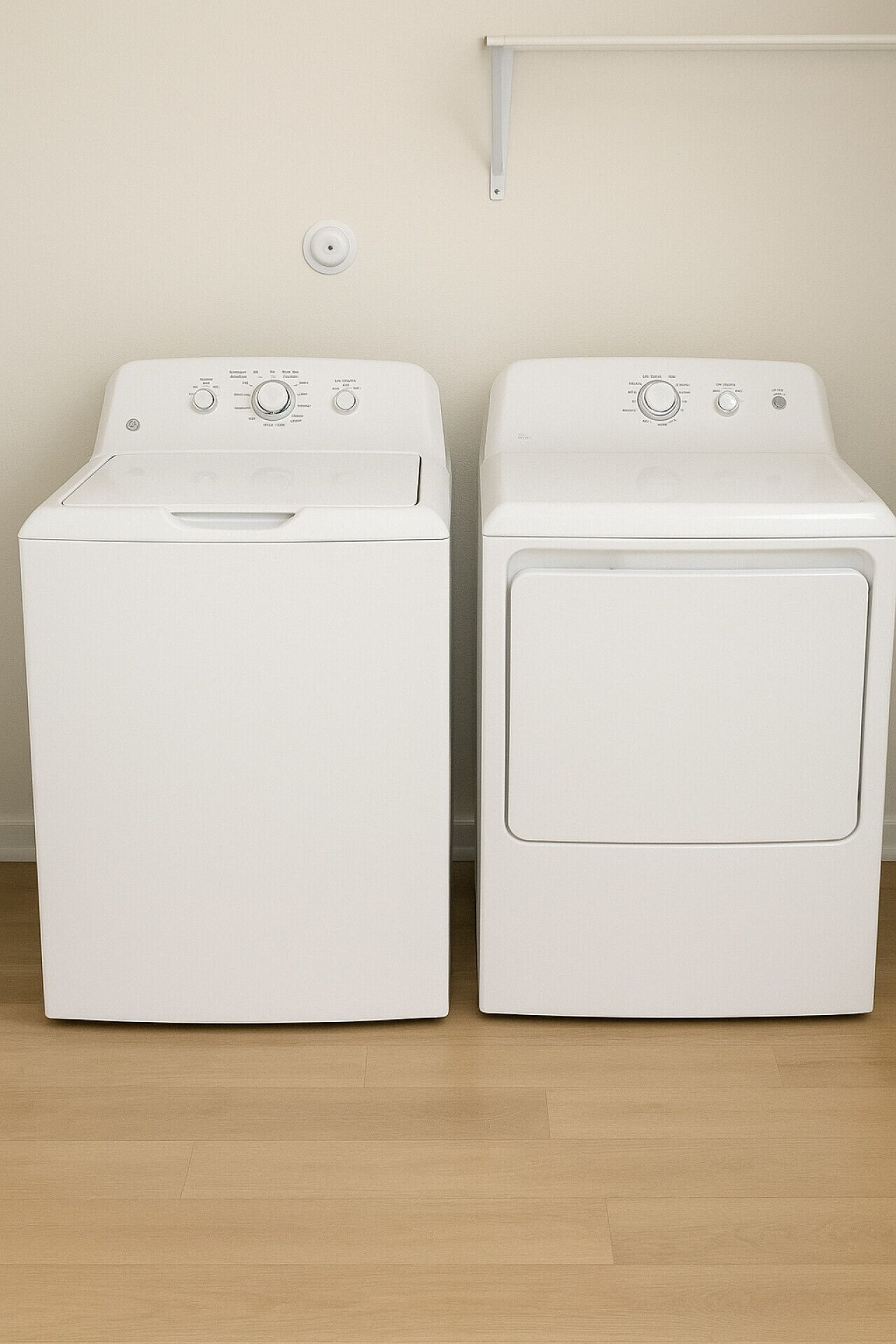Two white front-loading washing machines side by side on a wooden floor against a plain wall.
