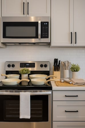 A kitchen with a stainless steel microwave, oven, and stovetop. There are two bowls on the stovetop, a plant, and a utensil holder. - GymPool Workerfriendly A+Location WashandDry (Sherman)