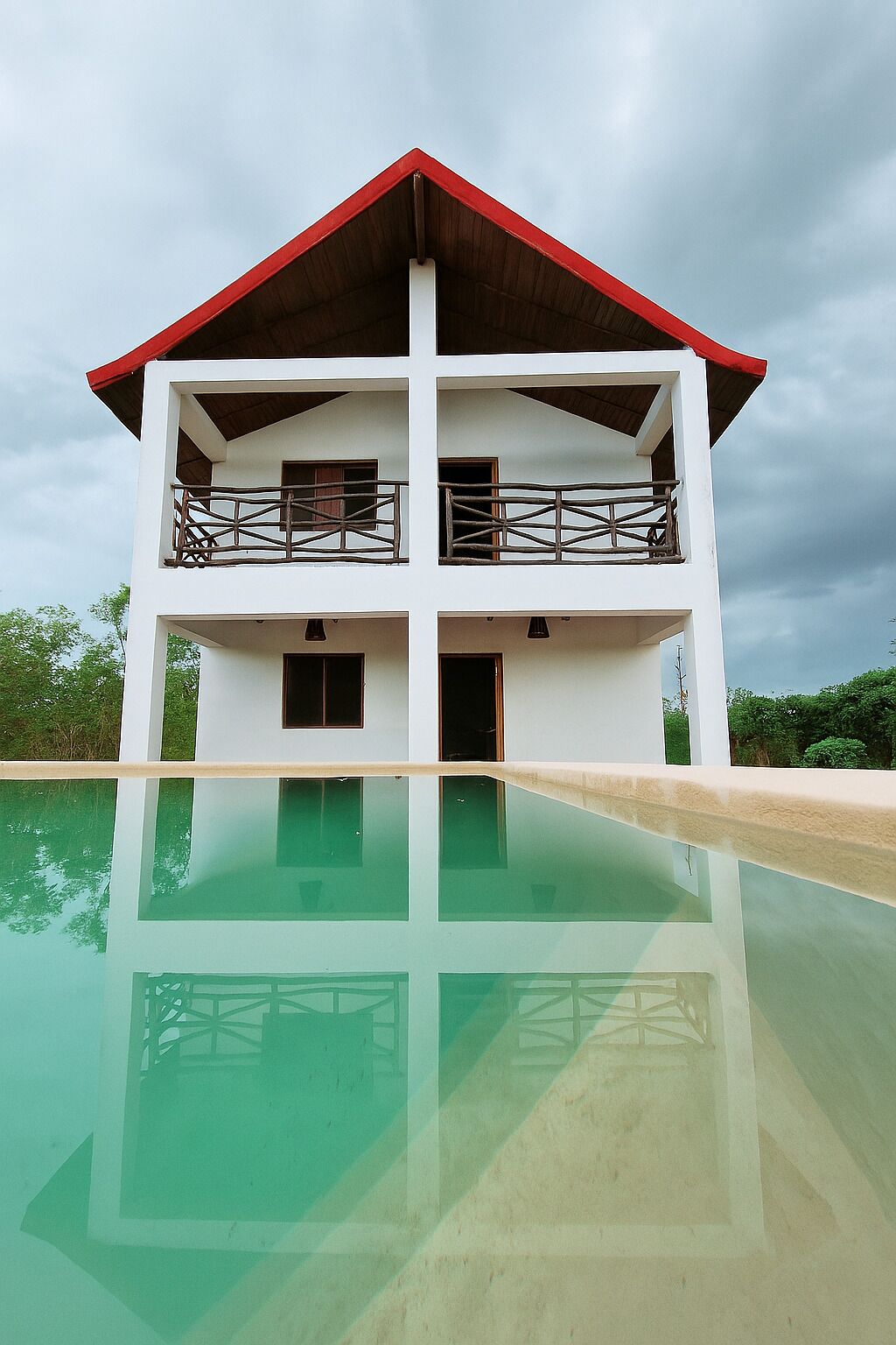 Un bâtiment à deux étages, avec un toit rouge et une piscine à l’avant.