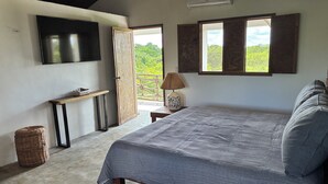 Ein Schlafzimmer mit Bett, einem an der Wand befestigten Fernseher, einem Fenster und einer Tür zu einem Außenbereich.