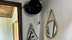 Ein Zimmer mit einem Waschbecken aus Holzschale, einem gestreiften Handtuch, einem Spiegel und einem schwarzen Ventilator.