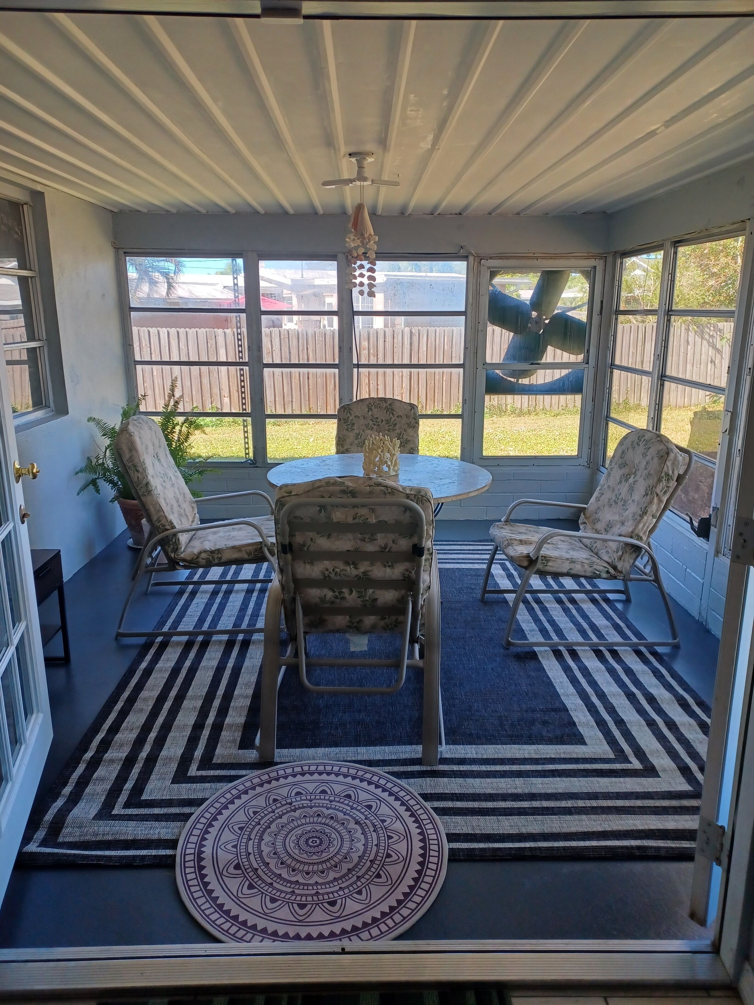Eine überdachte Terrasse mit rundem Tisch, zwei Stühlen und einem Deckenventilator.