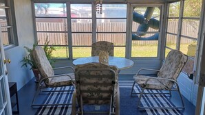 Une terrasse couverte avec une table ronde, deux chaises et un ventilateur de plafond.