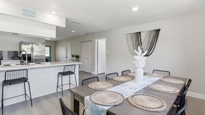 Een moderne keuken met een centraal eiland, een eethoek met een grote tafel en stoelen, en uitzicht op een strand.