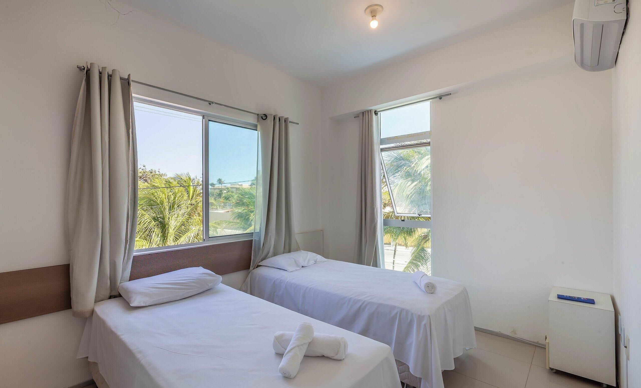 A hotel room with two single beds, a small table, and a window with curtains.
