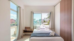 A hotel room with a bed, a small seating area, and a large window offering a city view. - Apart With 2 Bedrooms, 150m From the Beach Kvd0201 (Caucaia)