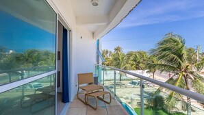 A balcony with a wicker chair, a glass railing, and a view of palm trees and a parking lot. - Apart With 2 Bedrooms, 150m From the Beach Kvd0201 (Caucaia)