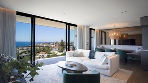A modern living room with a white sofa, a coffee table, and a view of the city and sea. - Sky Penthouse, Tamarama (Tamarama)