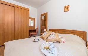 Une chambre à coucher comprenant un lit, une armoire en bois, une chaise, une table de chevet et un petit miroir.