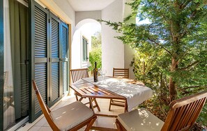 Une terrasse avec une table et des chaises en bois, une bouteille de vin et un verre.