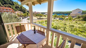Un balcón con mesa y sillas, con vistas a un paisaje pintoresco que incluye una masa de agua y edificios al fondo.