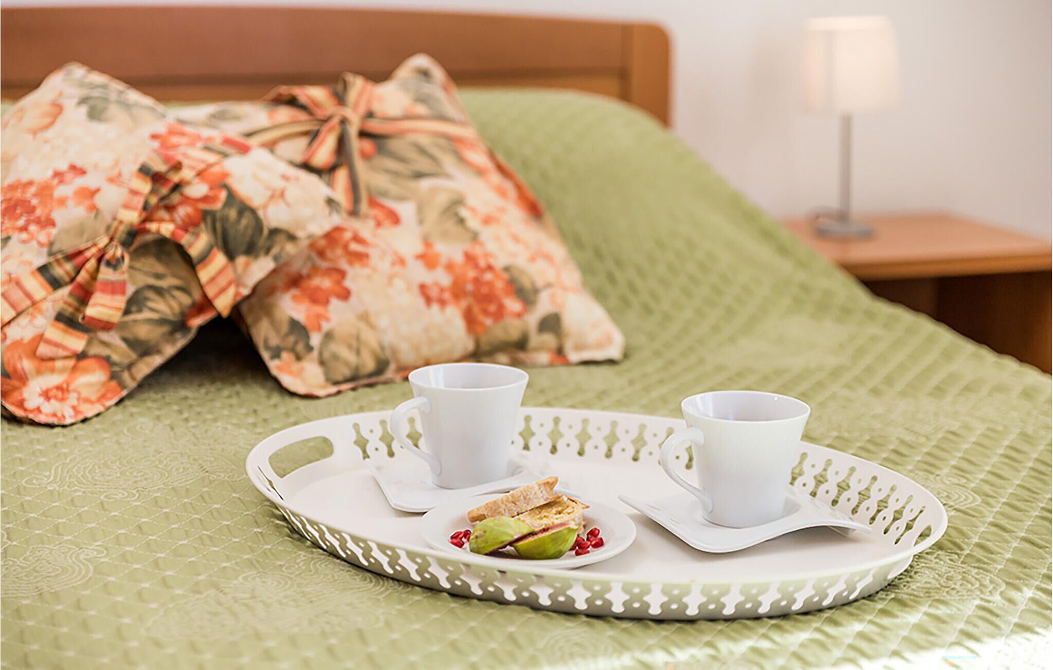 En pænt anrettet bakke med morgenmad, to kopper og en sandwich på et gr ønt lagen.