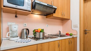 A compact kitchenette with a microwave, kettle, and stove, wooden cabinets, and a fruit bowl on the counter.