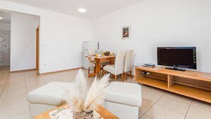 Ein modernes Wohnzimmer mit Essbereich, einem Flachbildfernseher und einer kleinen Küche im Hintergrund.