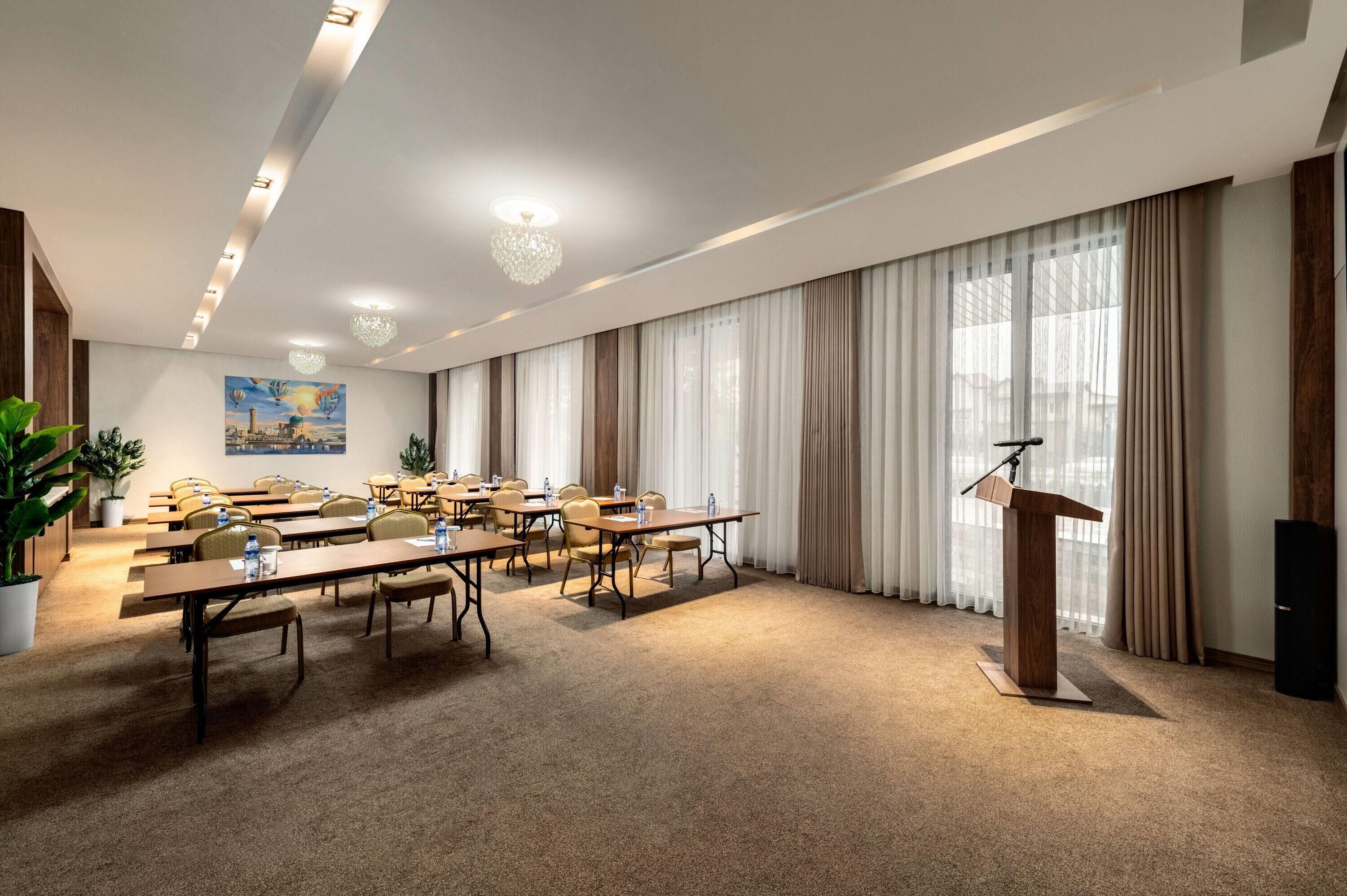 Une salle de conférence équipée d’un pupitre, de tables, de chaises et d’une grande fenêtre avec des rideaux.