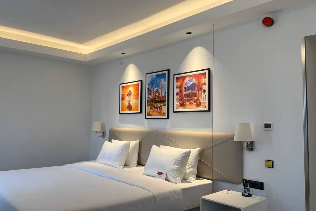 A hotel room with a bed, bedside lamps, a phone, and three framed pictures on the wall.