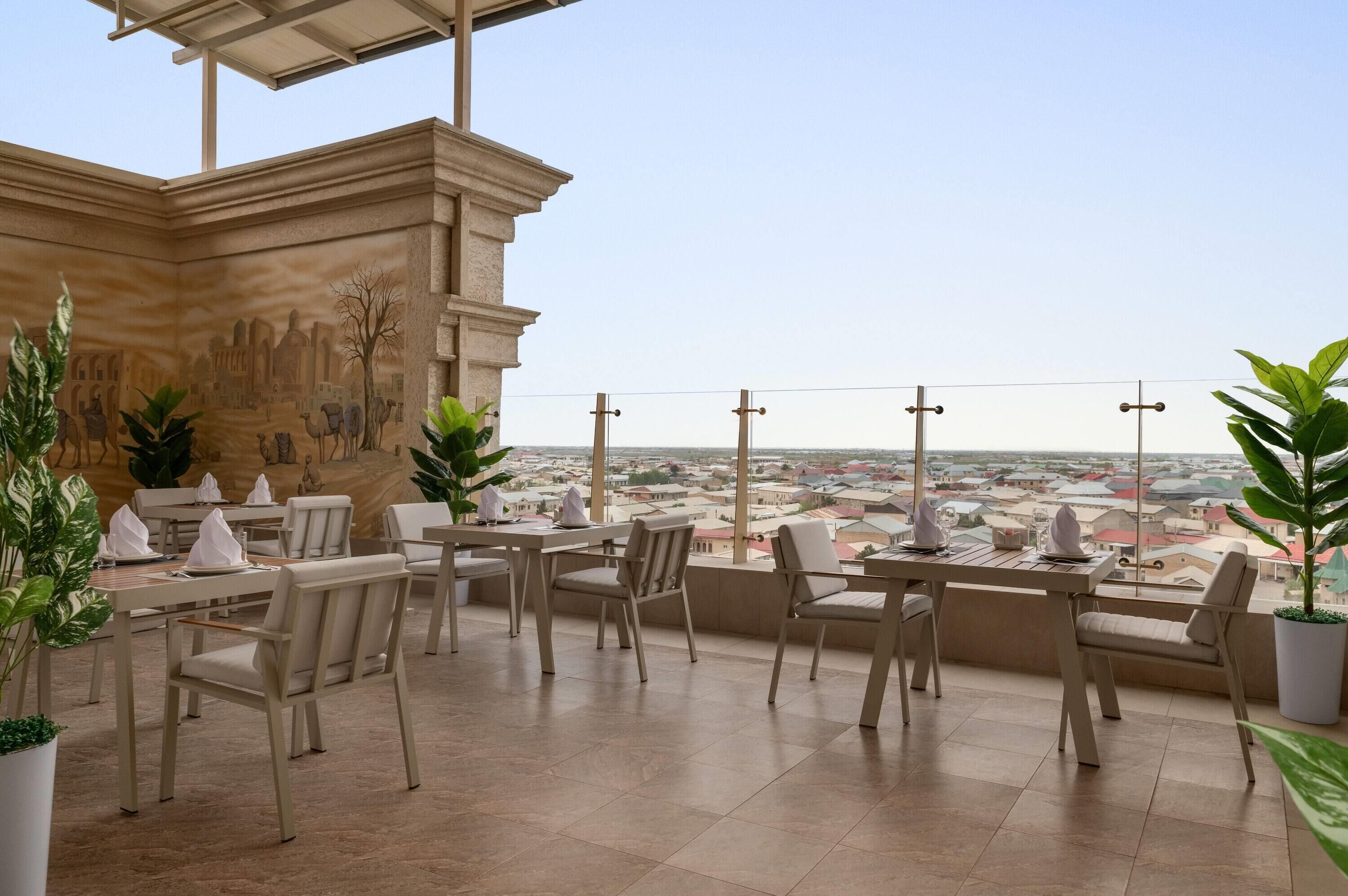 Un espace extérieur aménagé pour les repas, avec des tables et des chaises, une fresque murale et une vue sur le paysage urbain.