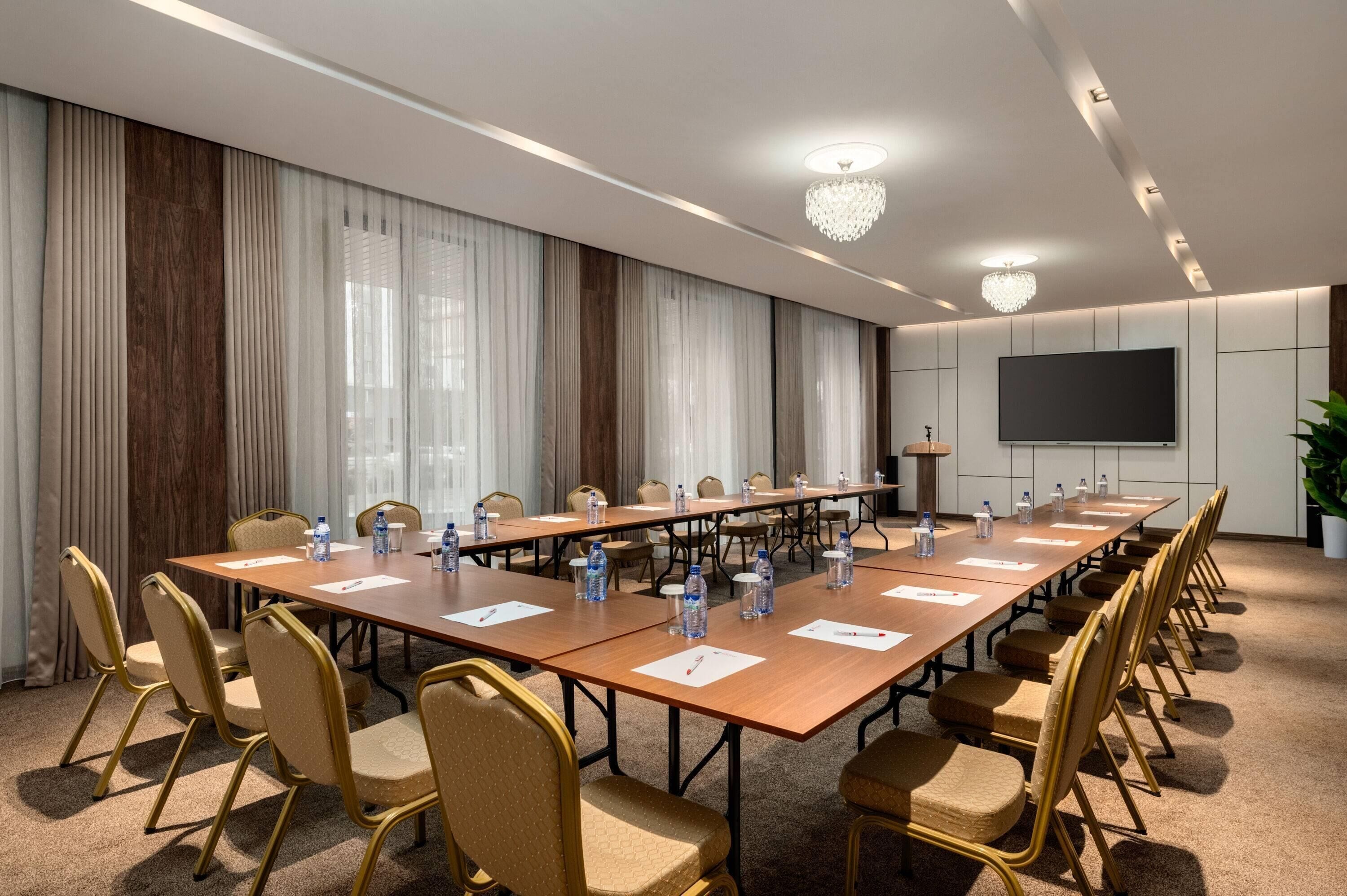 A conference room with a long table, chairs, water bottles, and a projector screen.
