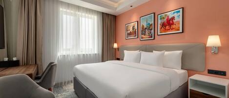 A hotel room with a large bed, a desk, a chair, and two wall-mounted lamps.