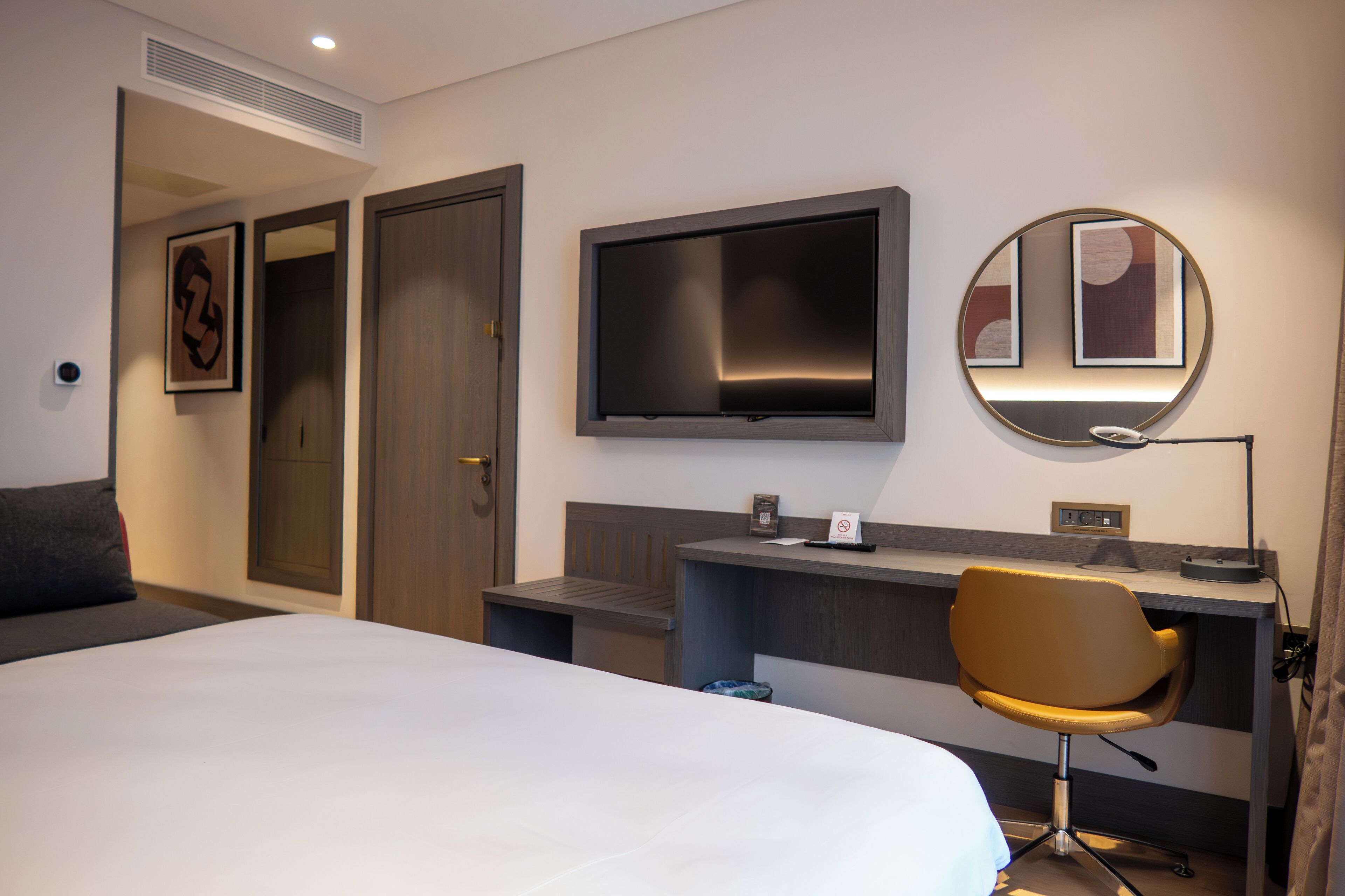 Una habitación de hotel con cama, escritorio, silla, televisor y espejo.