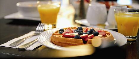 A breakfast setting with a waffle topped with strawberries and blueberries, a glass of orange juice, and a fork and knife on a napkin.