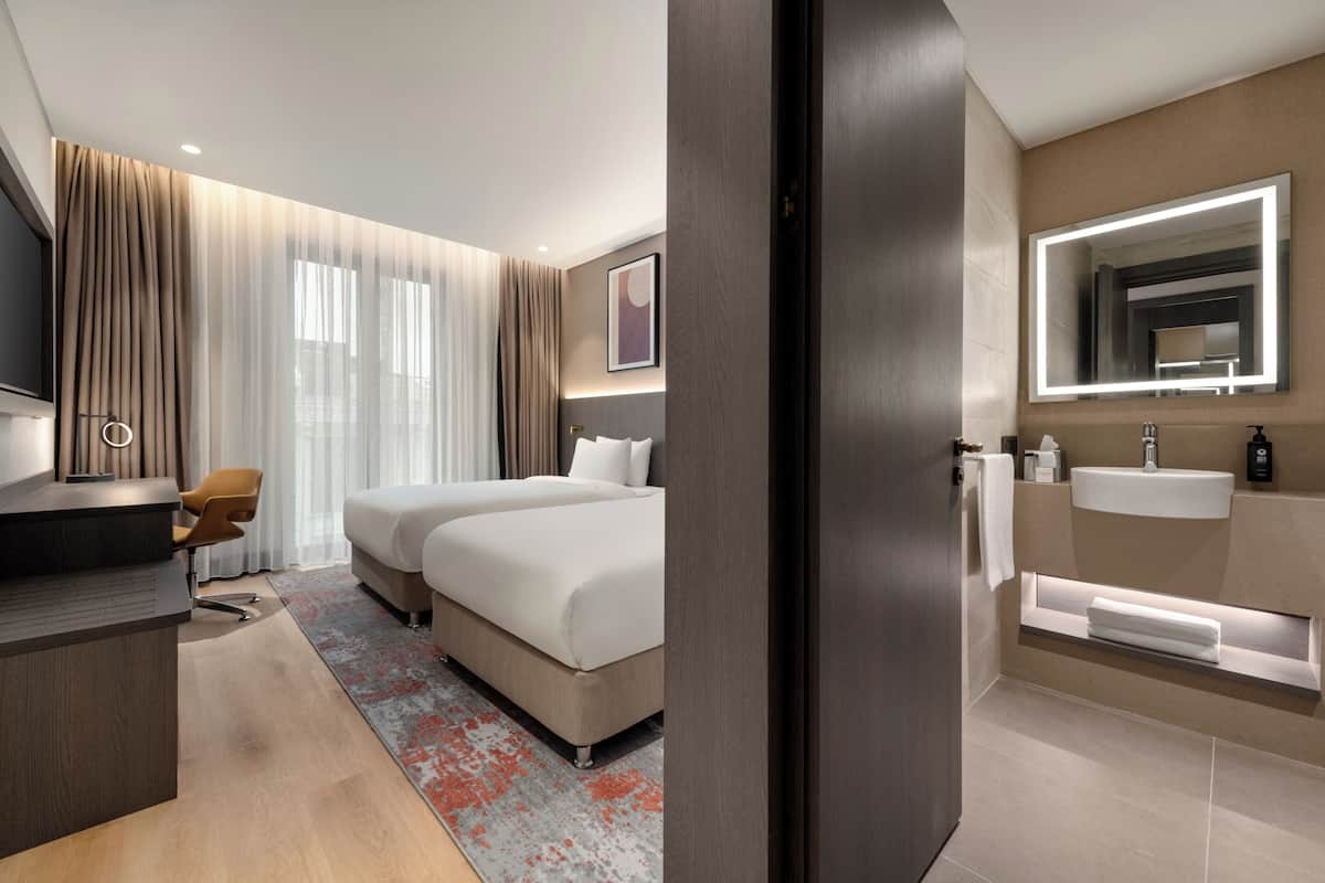 Una habitación de hotel con cama, escritorio, silla y baño con lavamanos y espejo.