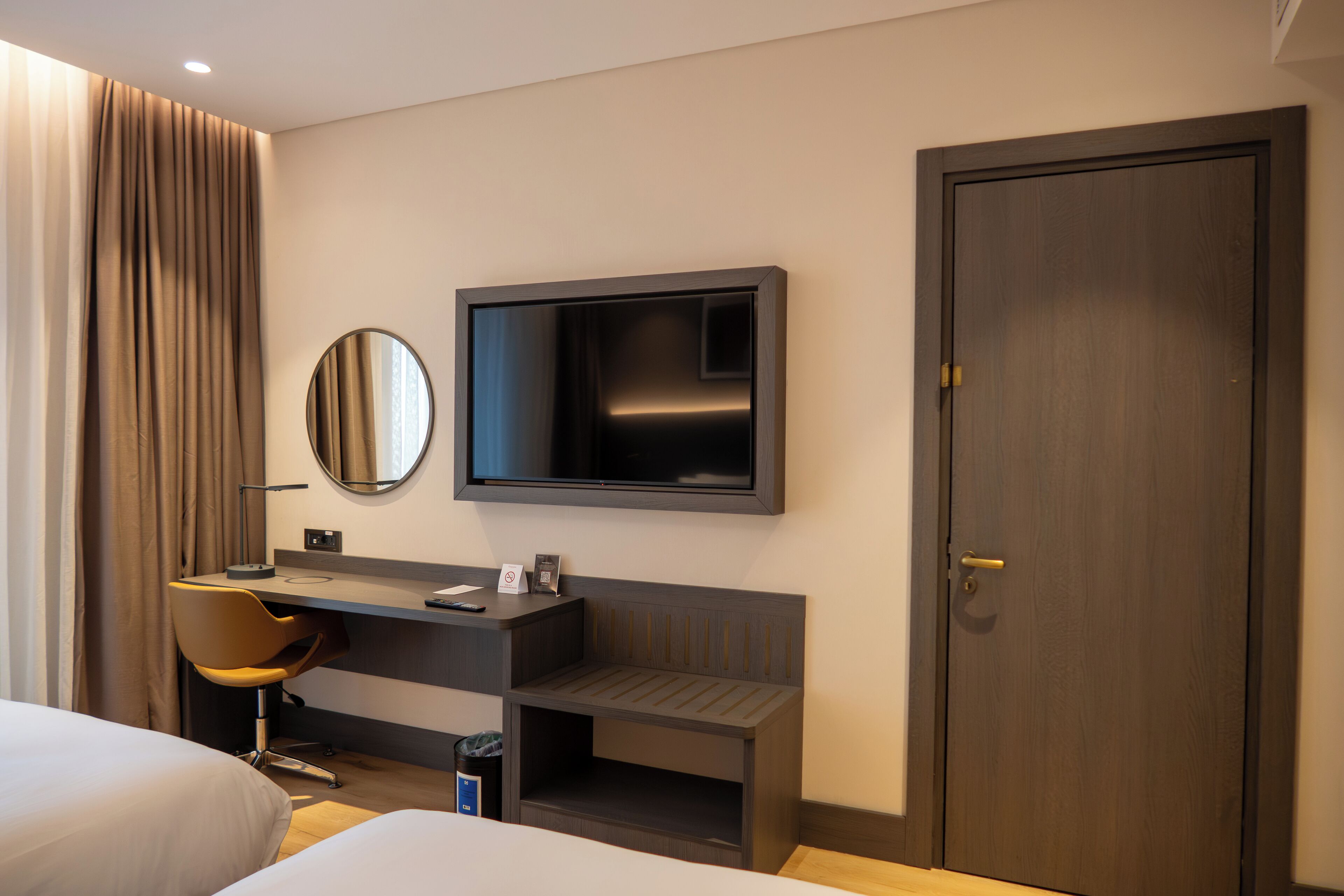 Een moderne hotelkamer met een bed, een bureau met stoel, een televisie en een deur.