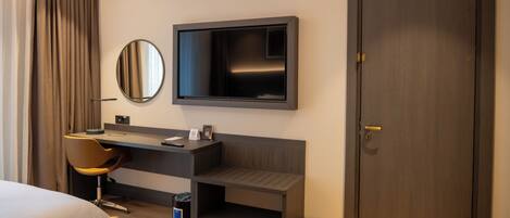 Una habitación de hotel moderna con una cama, un escritorio con una silla, un televisor y una puerta.