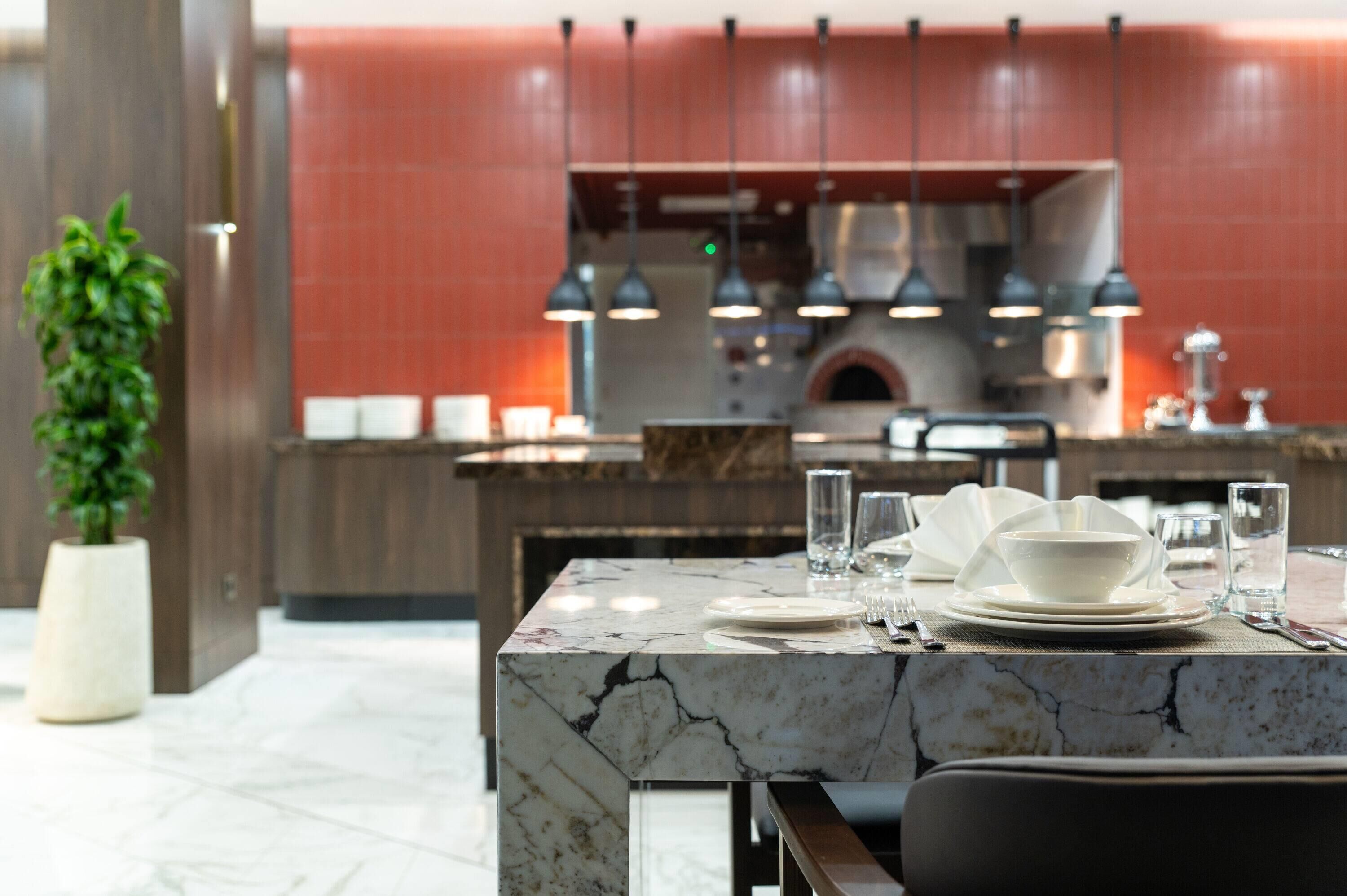 A modern kitchen with a marble countertop, overhead lighting, and a red-tiled backsplash.