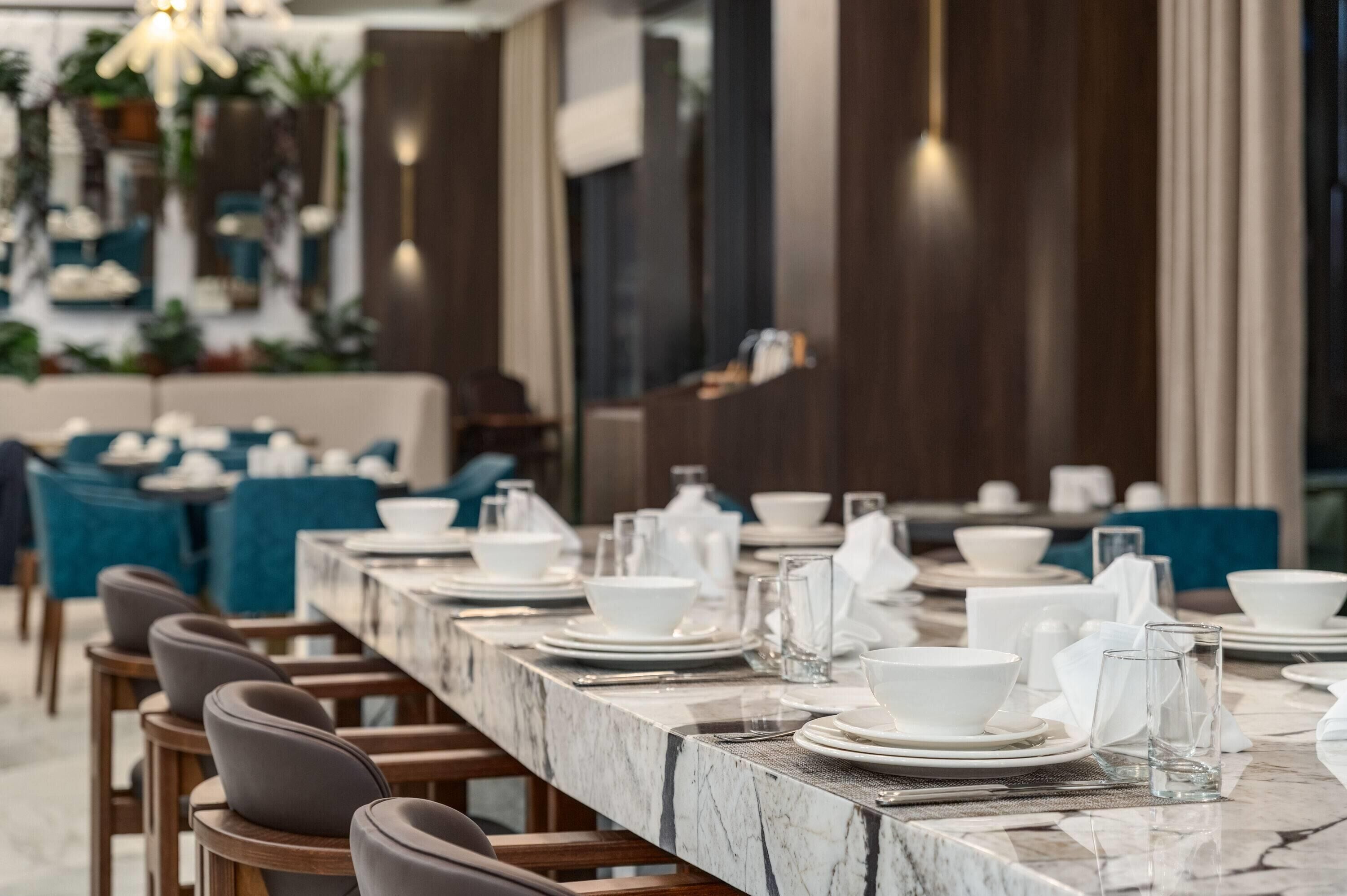 A restaurant with a long marble counter, blue upholstered chairs, and white table settings.