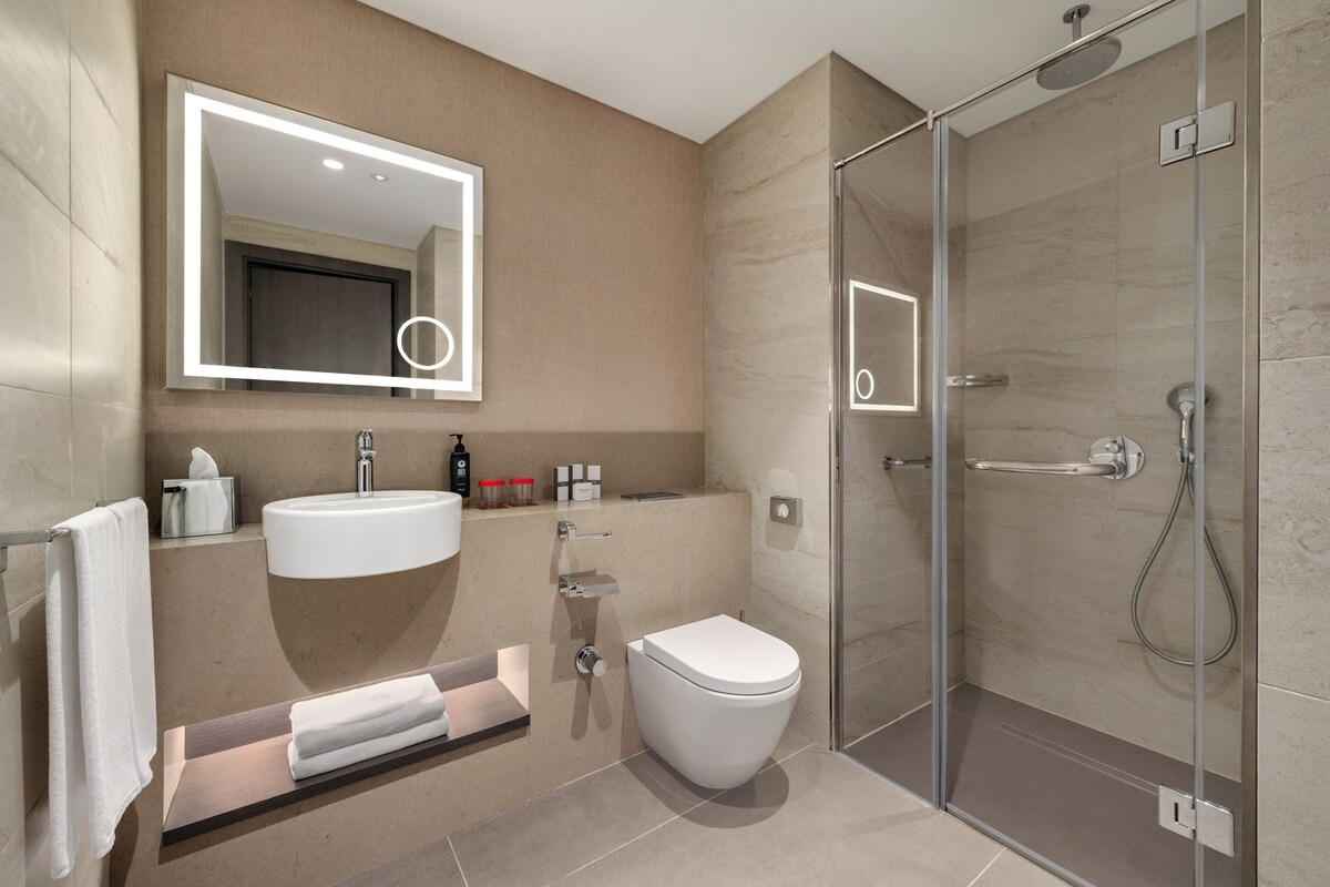Un baño moderno con ducha envuelta en vidrio, un lavamanos blanco y un inodoro.