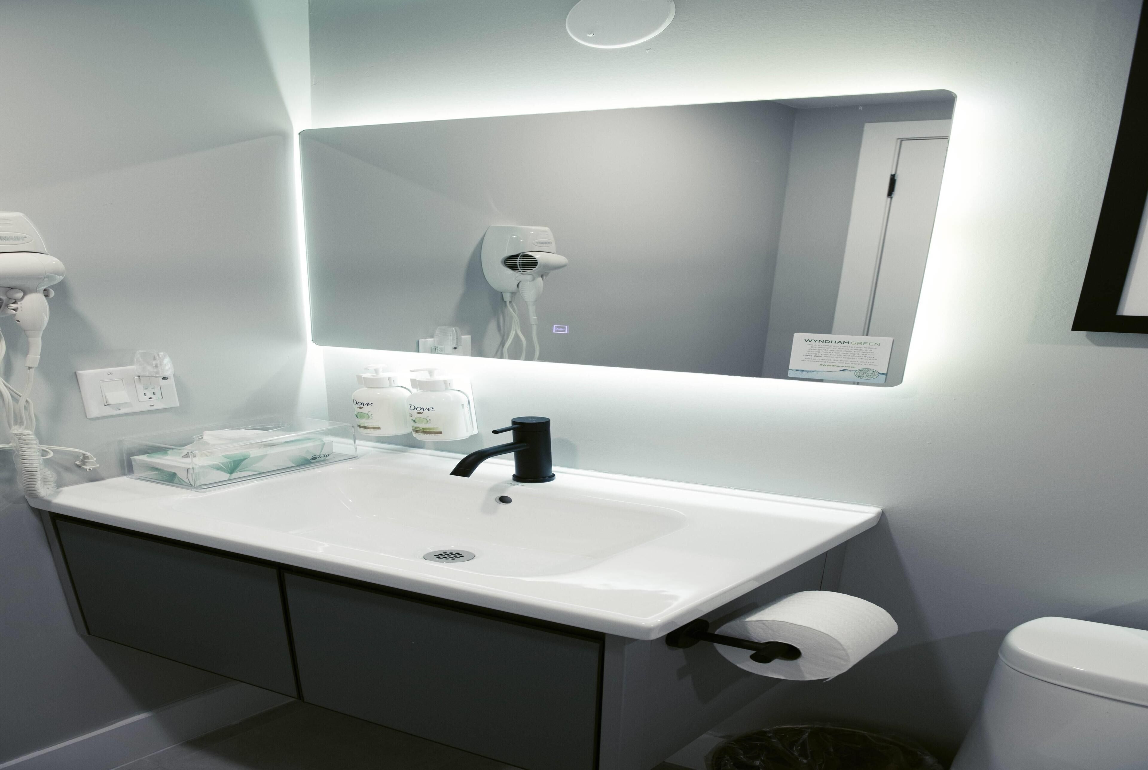 A bathroom with a white sink, a mirror, a hairdryer, and a toilet.