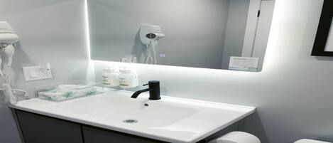 Une salle de bain avec un lavabo blanc, un miroir, un sèche-cheveux et des toilettes.